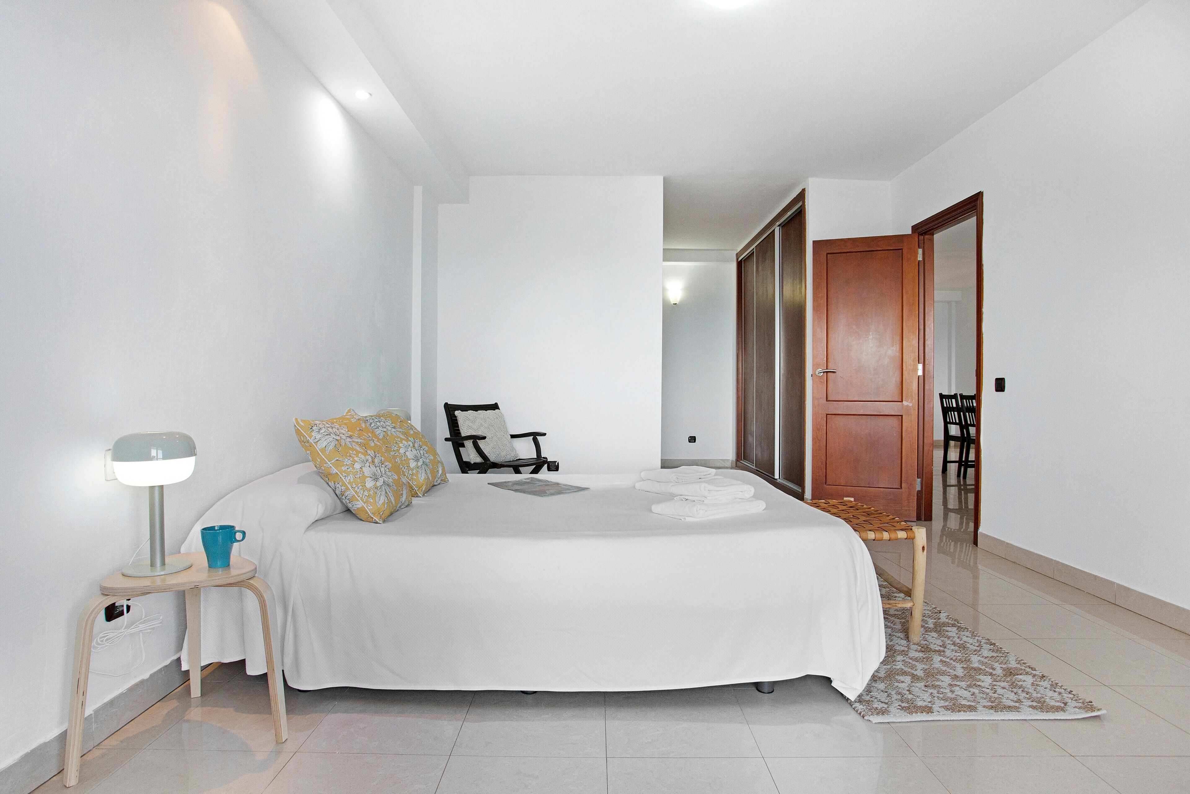 Une chambre à coucher comprenant un lit, une table de chevet, une lampe, une chaise et une porte donnant sur une autre pièce.