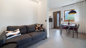 Un salon moderne avec un canapé, une table à manger et des chaises, un luminaire suspendu et une vue par la fenêtre.