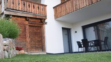 Un bâtiment doté d’un balcon en bois, d’une porte et d’un patio aménagé avec des chaises et une table.