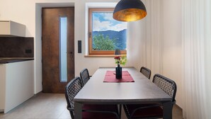 Un coin repas comprenant une table, des chaises, un vase de fleurs, un luminaire suspendu et une fenêtre donnant sur les montagnes.