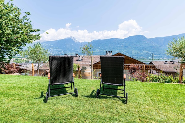 Zwei Gartenstühle aus Rattan, die auf eine gebirgige Landschaft mit Blick auf ein Gebäude mit einem Ziegeldach zeigen.
