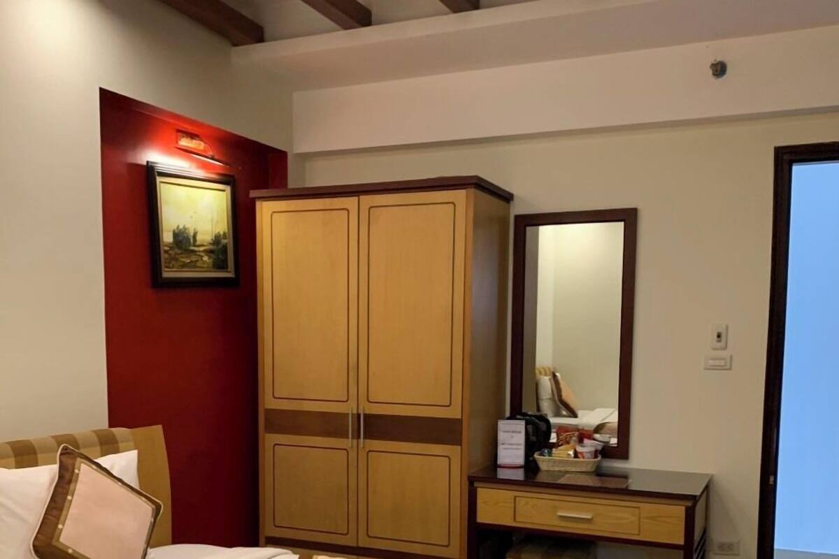 Ein Hotelzimmer mit einem großen Bett, einem Holzschrank, einem Schreibtisch mit Spiegel und einer roten Akzentwand.