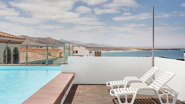 A rooftop pool with white lounge chairs, a clear view of the ocean, and mountains in the distance. - Vacation Studio 'Estudio Vista Mar 5' with Sea View, Shared Pool and Wi-Fi (El Cotillo)