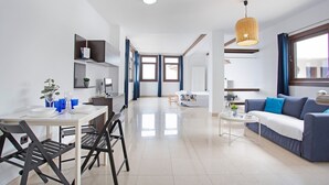 A modern living room with a sofa, a dining table with chairs, a coffee table, and a hanging light fixture. - Vacation Studio 'Estudio Vista Mar 5' with Sea View, Shared Pool and Wi-Fi (El Cotillo)