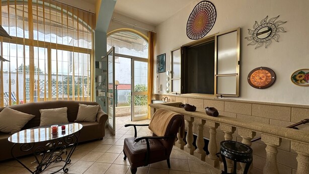 A room with a sofa, a table, a chair, a fireplace, and a view through large windows.