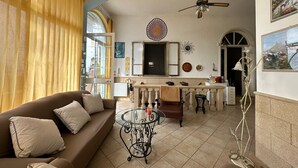 A living room with a sofa, a glass coffee table, a ceiling fan, and a kitchen area with a dining table and chairs.