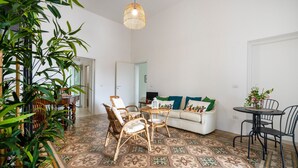 Ein Zimmer mit einem gemusterten Boden, einer Couch mit Kissen, einem Esstisch mit Stühlen und einer hängenden Leuchte.