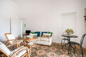 A room with a white sofa, wicker chairs, a round table, and a patterned floor.