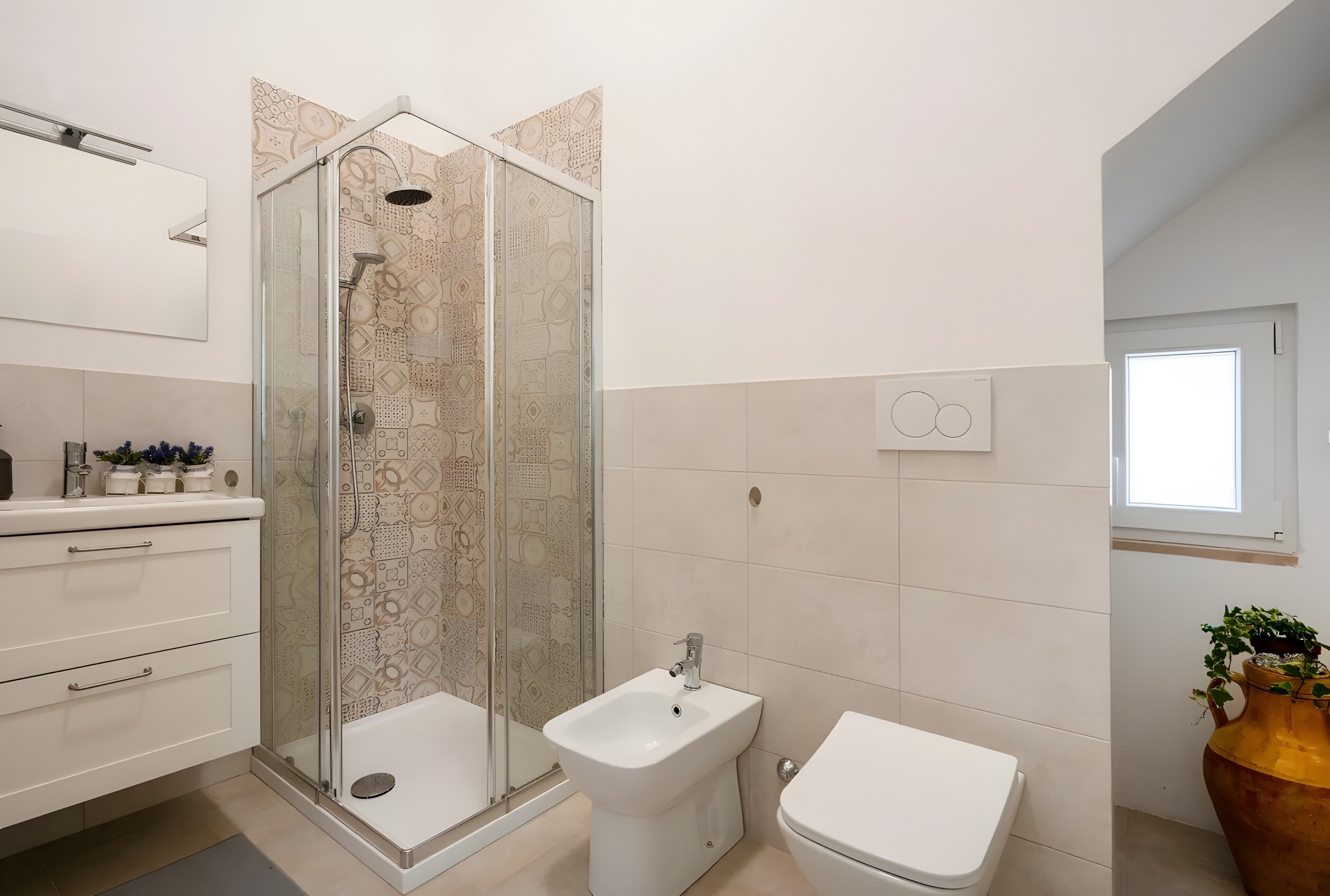 A bathroom with a shower enclosure, bidet, toilet, and a window.
