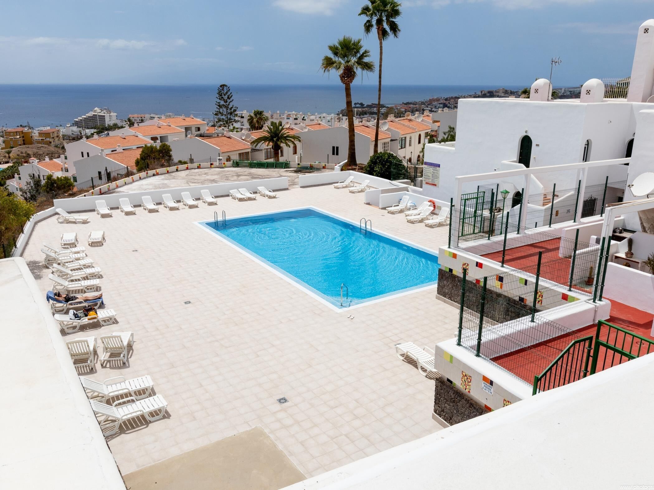 Une piscine sur le toit, dotée de chaises longues, offrant une vue sur la mer et sur les bâtiments blancs.