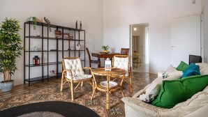 A living room with a dining area, a bookshelf, wicker chairs, a patterned floor, and a sofa with green cushions. - Stella — Apartment with Kitchen, Garden & Air Conditioning in Monopoli (Monopoli)