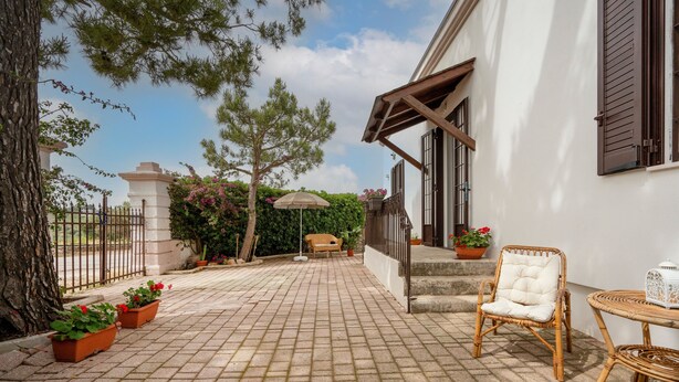A paved patio with potted plants, a wicker chair, and a small table. - Stella — Apartment with Kitchen, Garden & Air Conditioning in Monopoli (Monopoli)