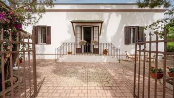 A white building with a brick-paved entrance, a gated porch with potted plants, and a clear sky.