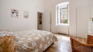 A bedroom with a bed, a wicker chair, a wardrobe, a window with a view, and two framed pictures on the wall. - Stella — Apartment with Kitchen, Garden & Air Conditioning in Monopoli (Monopoli)