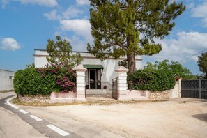Un bâtiment blanc surmonté d’un toit vert, doté d’une entrée fermée par un portail et d’un mur en pierre.
