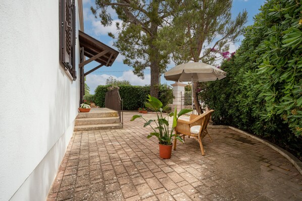 Une terrasse avec une table et des chaises, une plante en pot et un grand parasol.