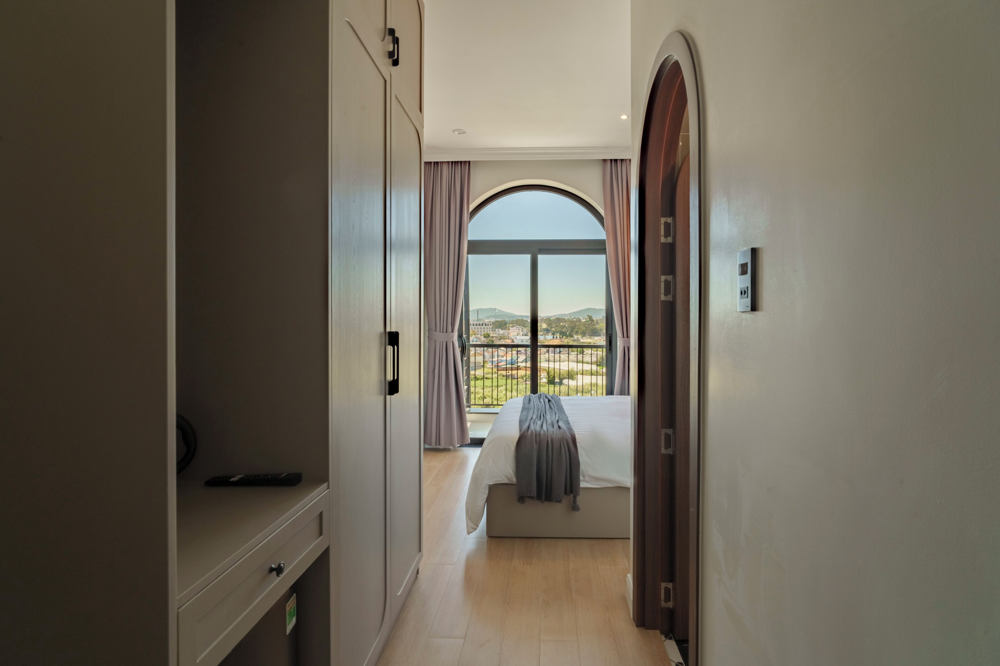 A bedroom with a large window, a bed, a bedside table, and a wardrobe.