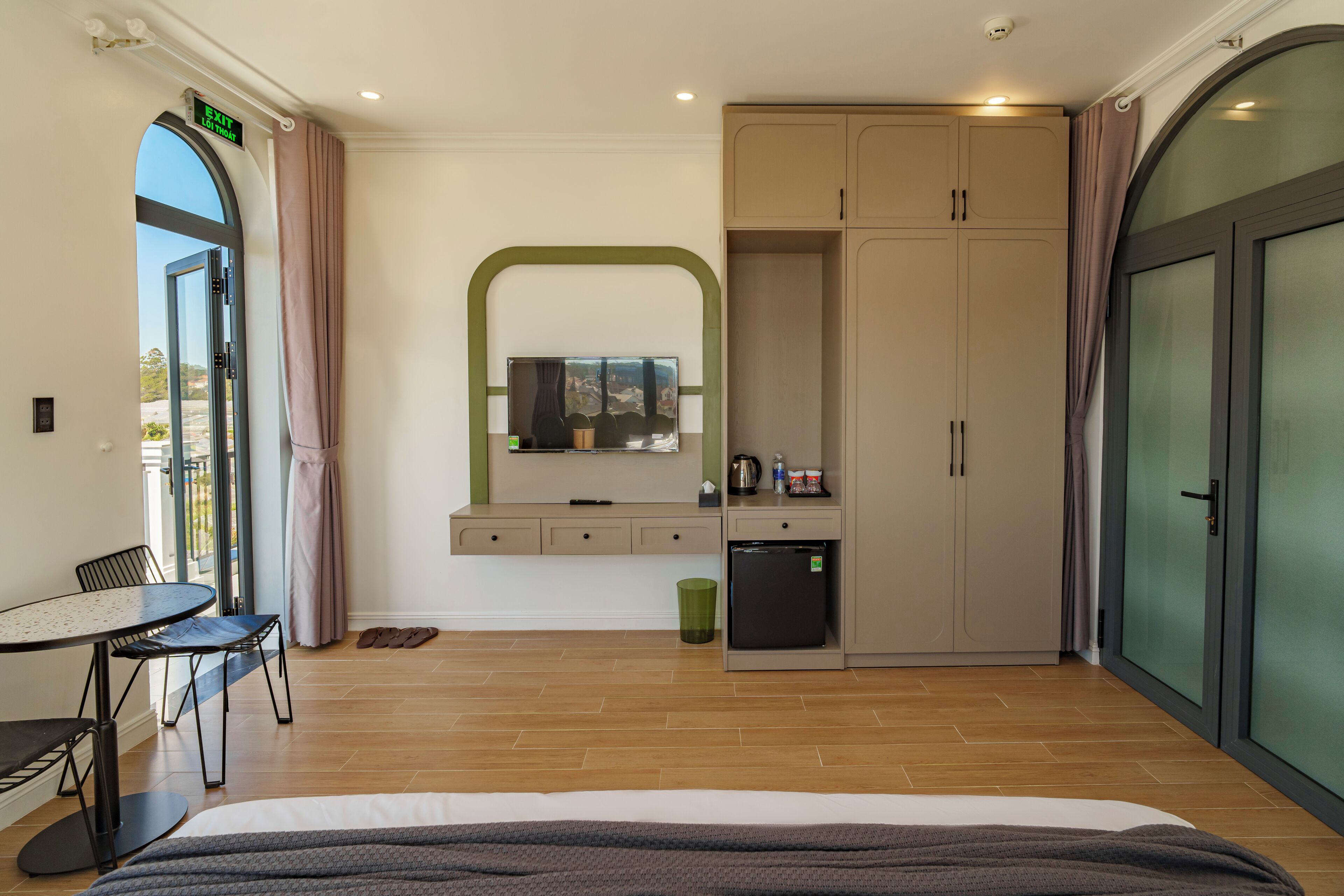 A hotel room with a bed, a desk, a small kitchenette, and a large wardrobe.