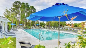 Une piscine entourée d’arbres et d’un bâtiment, avec des chaises longues et des parasols.