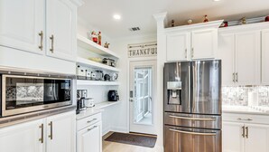 Une cuisine moderne avec des meubles blancs, des appareils en acier inoxydable et un panneau décoratif sur le mur portant l’inscription « Merci ».