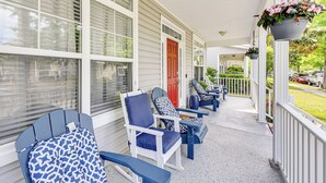 Une véranda avec des fauteuils Adirondack bleus et blancs, une porte rouge et des jardinières suspendues.