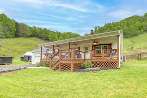 Ein zweistöckiges Haus mit überdachter Veranda, umzäunter Garten und hügeliger Landschaft im Hintergrund.