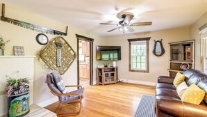 A living room with a wooden floor, a leather sofa, a chair, a television, and a decorative wall hanging. - Hike & Relax: Blue Ridge Mountain Retreat! (Burnsville)