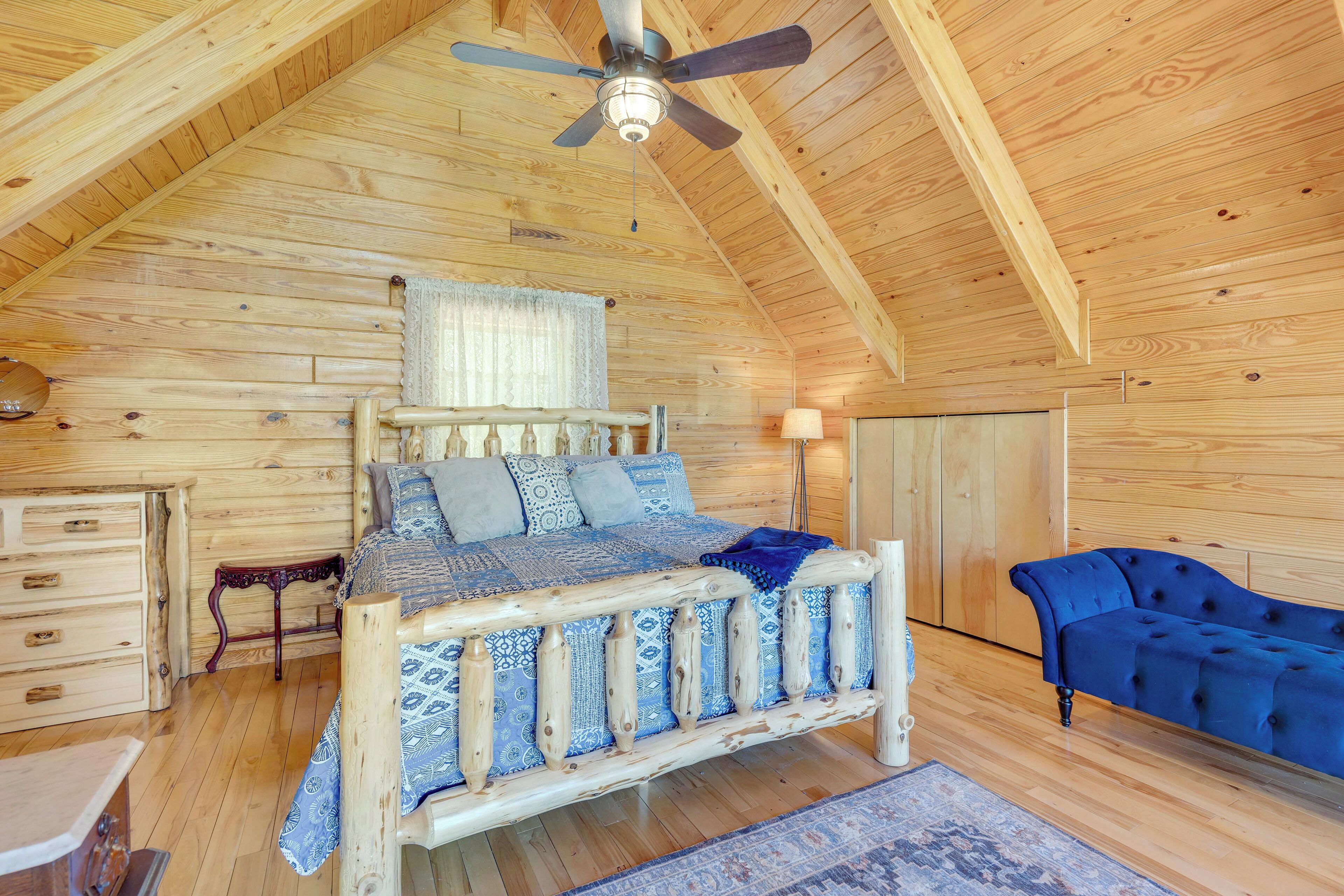 Une chambre à coucher en bois, avec un lit, un canapé bleu, un ventilateur de plafond et une commode en bois.