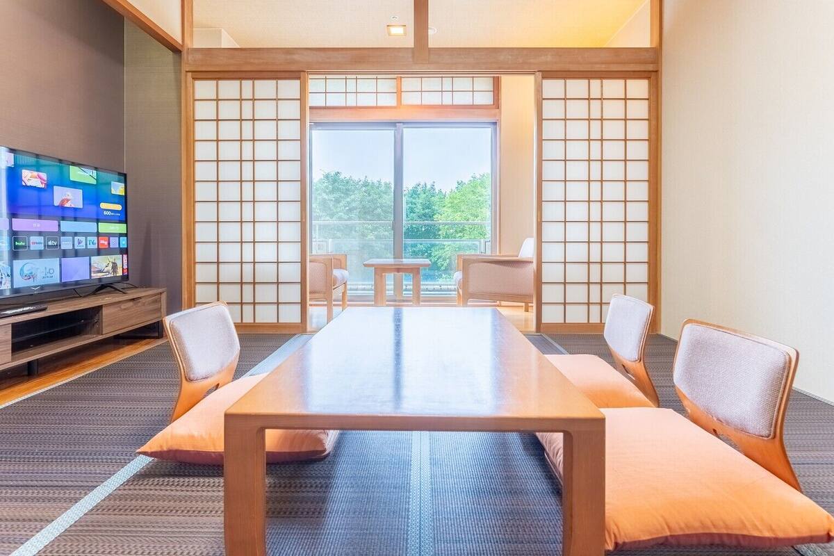 Een hotelkamer met een grote glazen schuifpui, een flatscreen televisie, een houten tafel en twee comfortabele fauteuils.