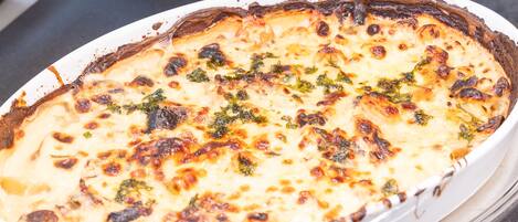 A white oval dish with a golden-brown crust, likely a baked dish with cheese and herbs, on a dark countertop.