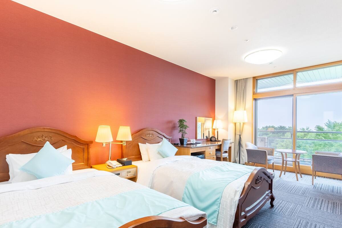 Een hotelkamer met twee bedden, een bureau, een stoel en een groot raam met uitzicht.