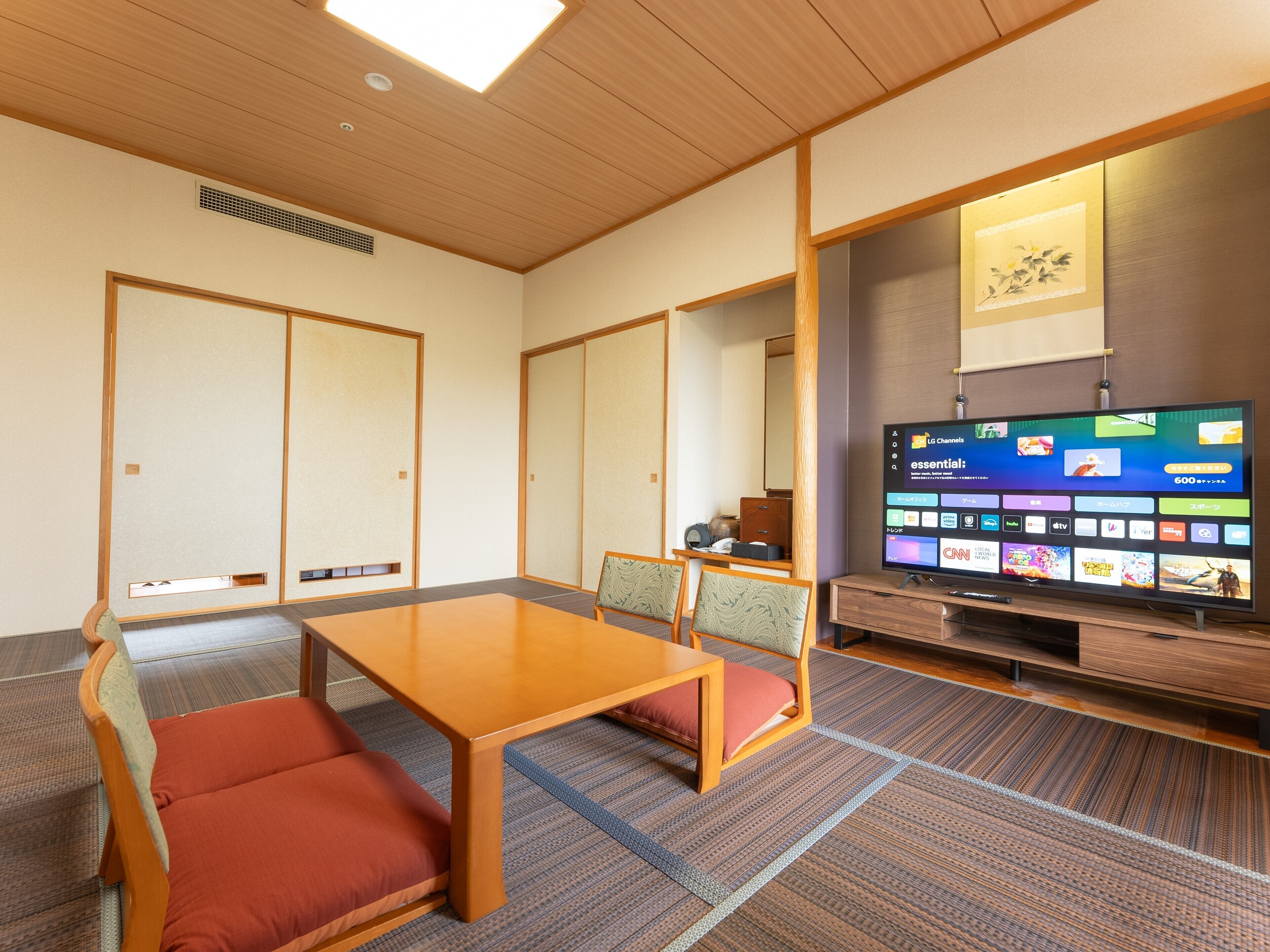 Habitación de hotel con techo de madera, suelo de esteras de tatami, televisor y puerta corredera tradicional japonesa.