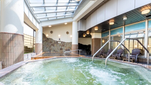 Ein Whirlpool mit Steinwand, Holzterrasse und Glasdach.