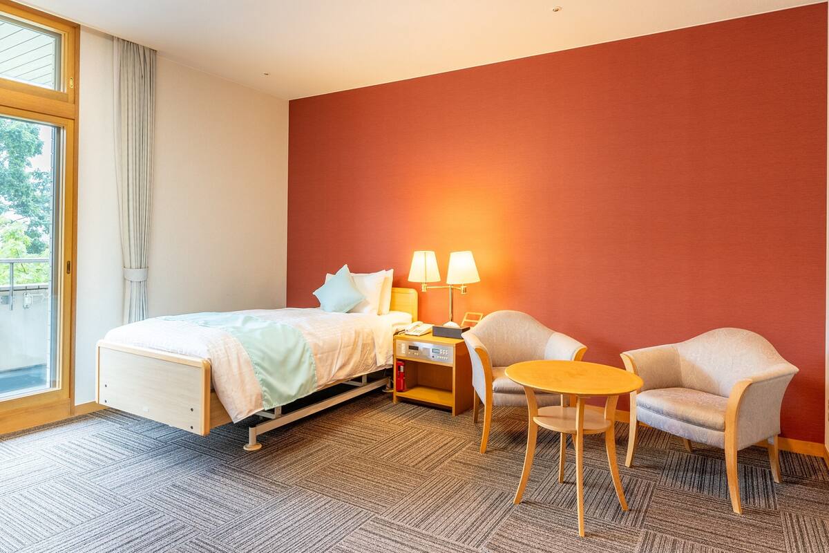 Een hotelkamer met een bed, twee stoelen, een kleine tafel en een nachtkastje met lampen.