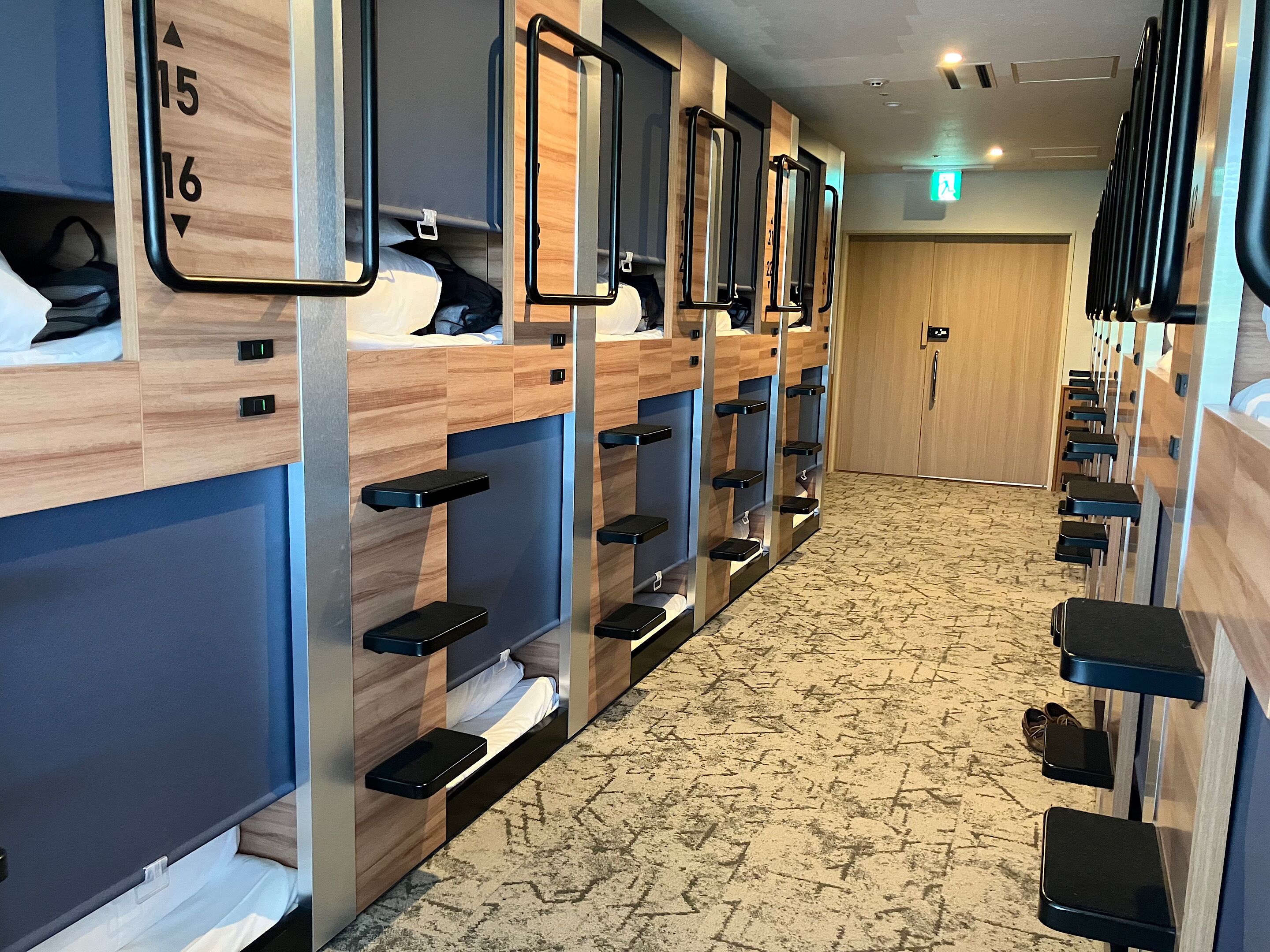 A hotel bathroom with multiple shower stalls, each with a wooden panel and a black shelf.