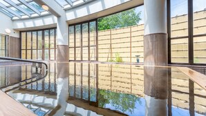 Ein moderner, überdachter Pool mit Glaswänden und einer Holzterrasse.