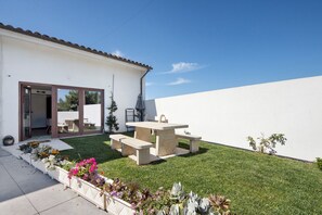 Un patio con tavolo e panche, un edificio bianco e un prato curato.