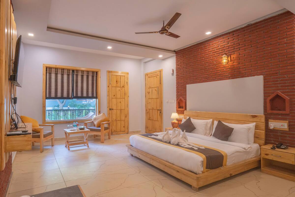 A hotel room with a large bed, a desk, a chair, and a window with blinds.