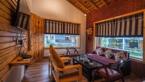 A cozy room with wooden walls, a sofa with cushions, a dining table, and two windows with striped curtains. - Destin Ekaant Resort by 3Tree Group (Ramnagar)