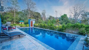 A swimming pool with lounge chairs and a small building, surrounded by trees and greenery. - Destin Ekaant Resort by 3Tree Group (Ramnagar)