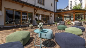 Un espace extérieur aménagé avec un sol en bois, des sièges rembourrés et une petite table sur laquelle est posé un vase.