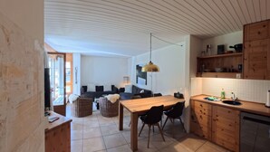 Une cuisine moderne avec une table à manger en bois, des chaises noires et un luminaire suspendu.