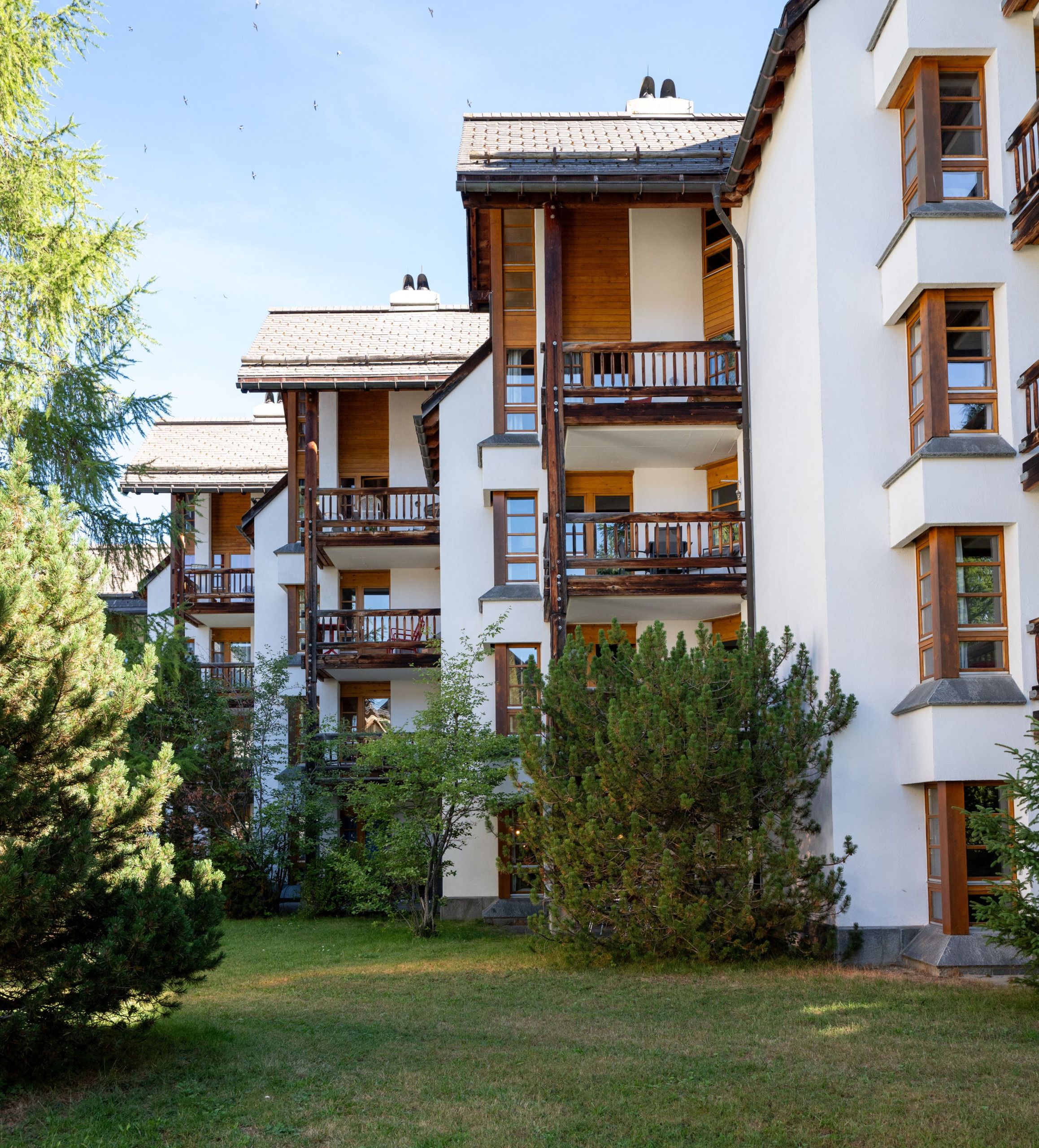 Un immeuble à plusieurs étages doté de balcons, d’un toit plat et entouré d’une zone verdoyante avec des arbres.
