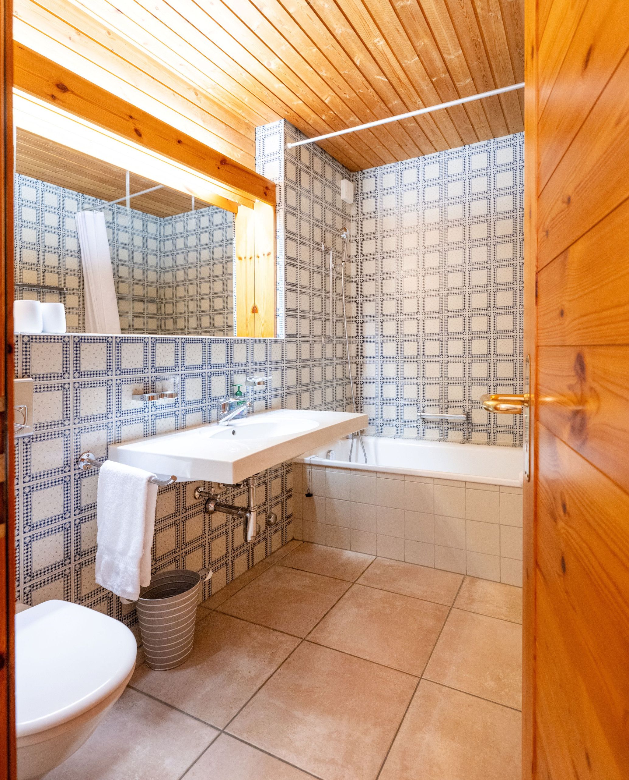 A bathroom with a wooden ceiling, patterned tiles, a white sink, a bathtub, and a toilet.