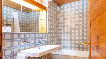 A bathroom with a wooden ceiling, patterned tiles, a white sink, a bathtub, and a toilet.