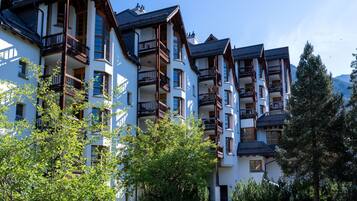 A row of multi-story buildings with balconies, surrounded by greenery and trees.