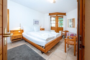 A bedroom with a wooden bed, bedside tables, a chair, a window with curtains, and a framed picture on the wall. - Wellness apartment with pool and terrace (Lenzerheide/Lai)