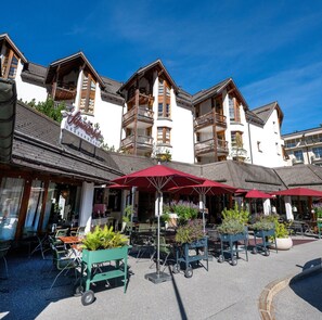 Un bâtiment de style européen traditionnel, doté de nombreux balcons, d’une terrasse avec des parasols rouges et d’une enseigne indiquant qu’il s’agit d’un restaurant.