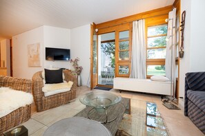 A cozy living room with wicker furniture, a glass coffee table, and a TV mounted on the wall. - Wellness apartment with pool and terrace (Lenzerheide/Lai)