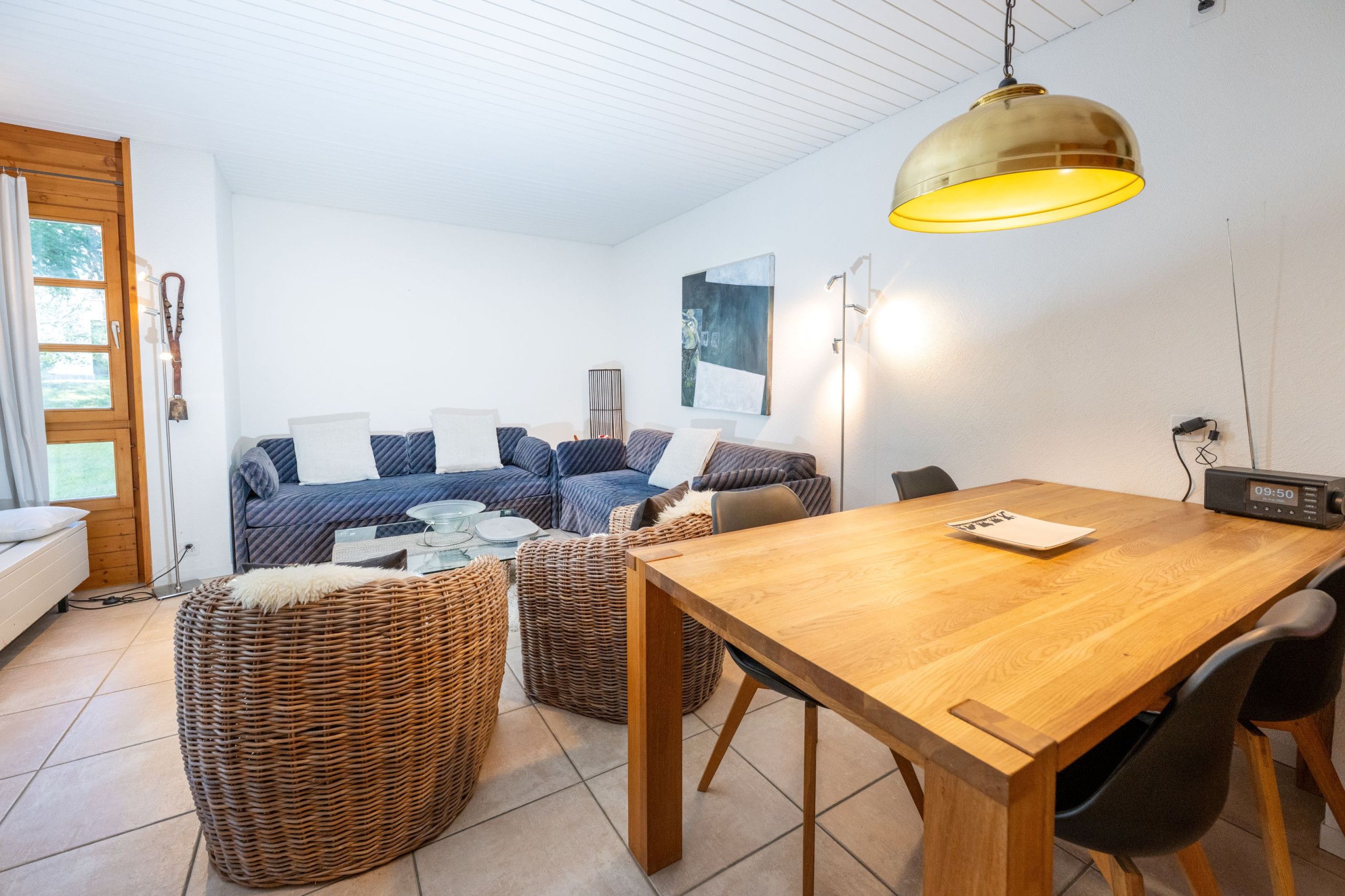 Un salon moderne avec une table à manger en bois, des poufs en osier et un canapé agrémenté de coussins.